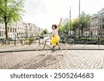 Happy woman riding a bicycle on the street of Amsterdam city - Delightful female tourist enjoying summer vacation in Europe landmark - Holidays, traveling and transportation life style concept