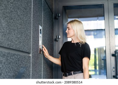 Happy Woman Ringing On Doorbell At Building Entrance. Using Intercom.