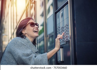 Happy Woman Ringing On Doorbell At Building Entrance. Using Intercom.