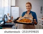 Happy woman roasting pumpkin while preparing Thanksgiving dinner int he kitchen and looking at camera.