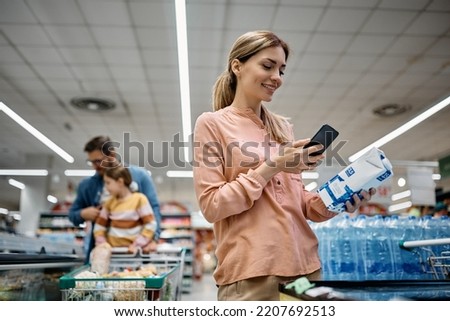 Happy woman scanning QR code on a product while shopping in supermarket.
