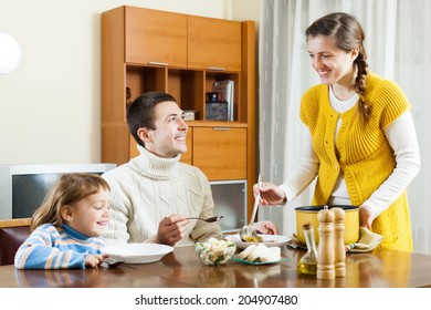 Happy Woman Serving Soup Her Husband And Child  In Home