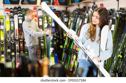 Happy woman shopper choosing new skis in shop of sports equipment