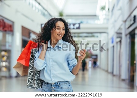 Happy woman shopping for clothes during the period of discounts and promotional offers, Hispanic woman smiling and happy browsing online discounts using smartphone, inside a modern large store.