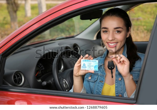 Happy\
woman showing driving license and key from new\
car