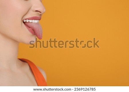 Happy woman showing her tongue on orange background, closeup. Space for text