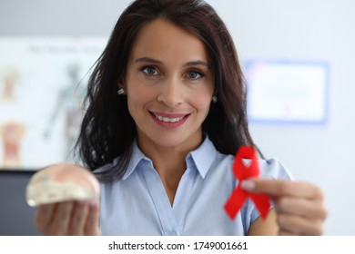 Happy Woman Shows Breast Implant And Red Ribbon. Way Out Critical Situation An Oncologically Ill Woman. Features Implantation After Breast Removal. Formation For Rehabilitation Treatment