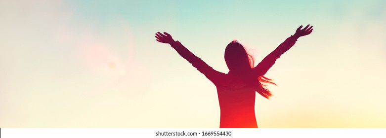 Happy woman sihouette with arms raised up in success on sunset glow sunshine banner panorama. Wellness, financial freedom, healthy life concept background.