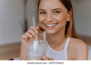 happy woman sipping milkshake in kitchen. Portrait of a happy young girl drinking coffee with milk. young girl smiling and drinking smoothie - Powered by Shutterstock