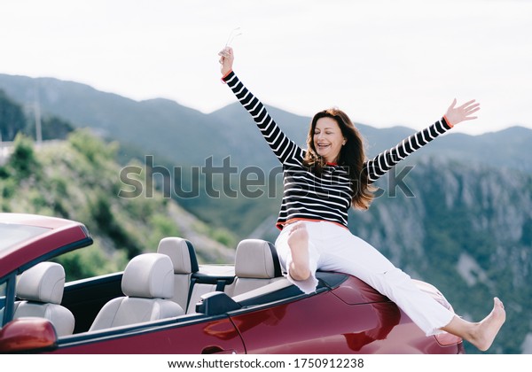 Happy woman sits in a red convertible car with a
beautiful view