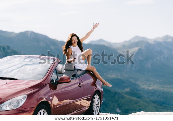 Happy woman sits in a red convertible car with a
beautiful view