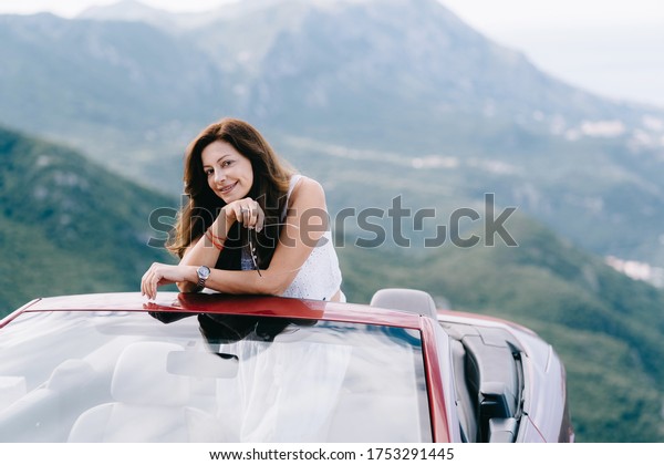Happy woman sits in a red convertible car with a\
beautiful view