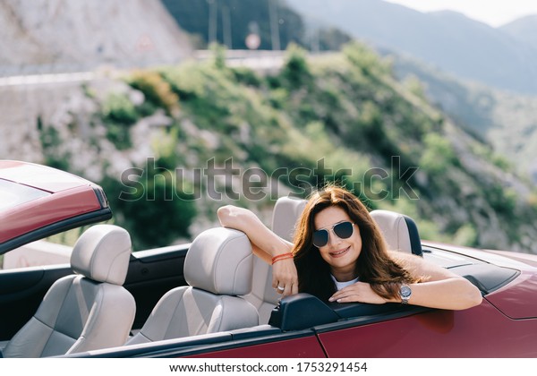 Happy woman sits in a red convertible car with a\
beautiful view