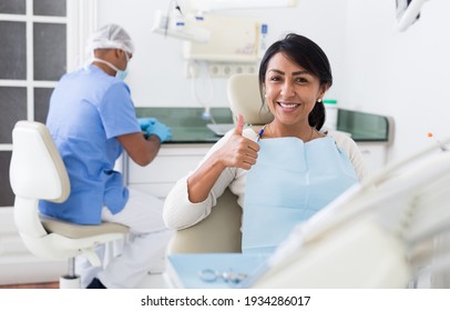 Happy Woman Sitting In Dental Chair After Teeth Cure Giving Thumb Up