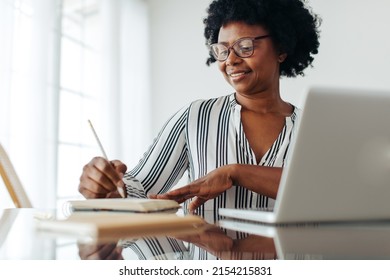 Happy woman sitting at desk at home and writing in her diary. Happy female taking notes in book while working from home.