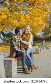 Happy Woman Sitting On Man's Lap At Park During Autumn