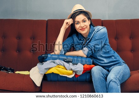 Happy woman sitting on sofa beside of travel suitcase with clothes.