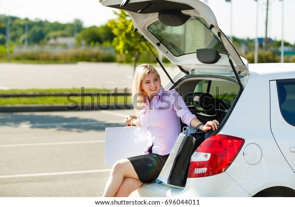 Happy woman sitting in an open trunk of a new\
car, smiling, joyfully safety comfort luxury travelling journey\
vacation automobile\
vehicle