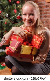 Happy Woman Sitting Under Christmas Tree With Pile Of Christmas Presents