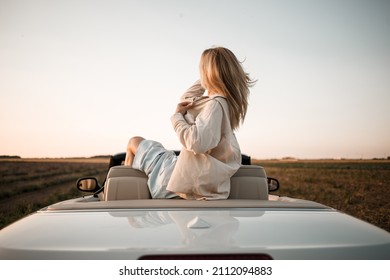 Happy woman sitting in white convertible car with beautiful view