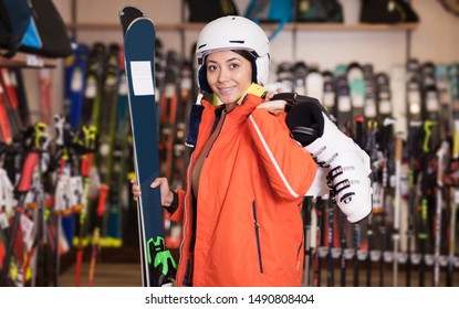 Happy woman in skiing outfit standing with purchased ski equipment in shop