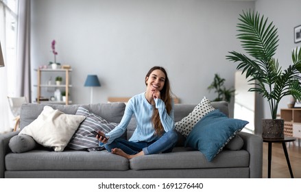 Fröhliche Frau mit Smartphone in zwangloser Kleidung auf dem Sofa. Träumen zu Hause.