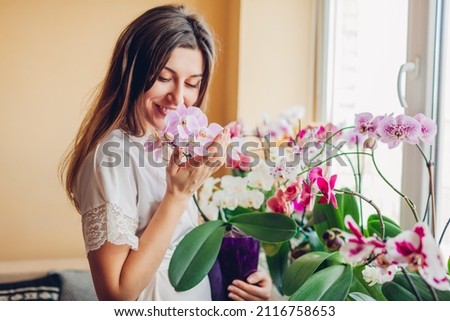 Happy woman smelling blooming purple orchid holding pot. Young girl gardener taking care of home plants and flowers enjoying hobby.