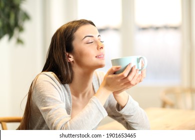 Happy Woman Smelling Coffee Aroma Sitting In A Table At Home