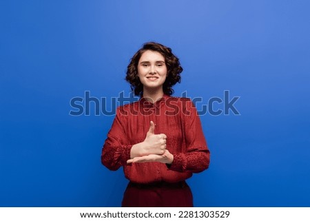 happy woman smiling at camera and showing help gesture on sign language isolated on blue