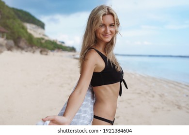 Happy Woman Smiling And Having Fun At Beach. Summer Portrait Of Young Beautiful Girl Running On Sandy Beach On Vacation, Turn Behind And Look At Camera, Wearing Black Bikini.