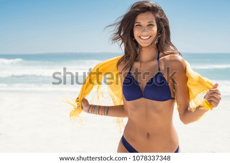 Happy woman smiling and having fun at beach. Summer portrait of young beautiful girl running on beach with a yellow scarf. Latin girl laughing and looking at camera with joy. 