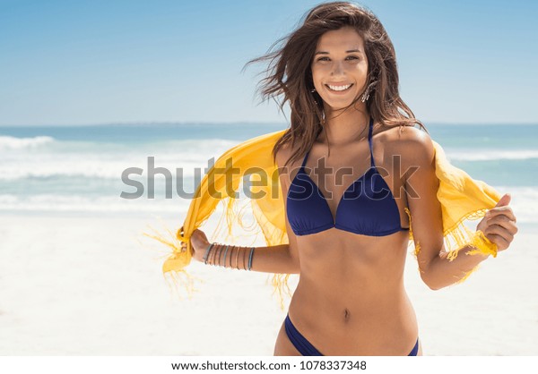 幸せな女性は笑顔でビーチで楽しんでいます 黄色いスカーフを持つビーチを走る若い美しい女の子の夏のポートレート 笑いながらカメラを見ながら喜ぶラテン女の子 の写真素材 今すぐ編集