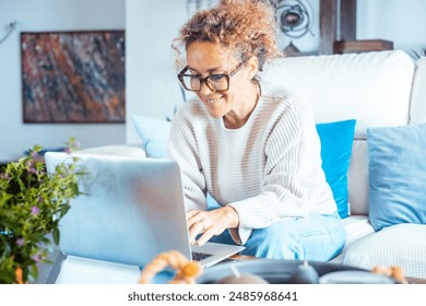 Happy woman smiling and writing on laptop sitting comfortable at home on the sofa wearing casual clothes. New business smart working concept lifestyle telecommuting. Cheerful lady using computer web - Powered by Shutterstock