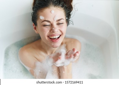 Happy Woman With Soap Suds On Her Face Lies In The Bathroom And Laughs