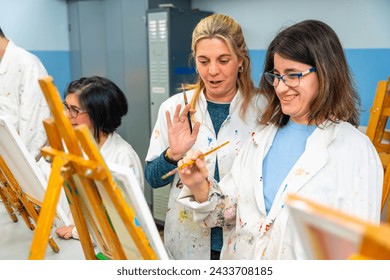 Happy woman with special needs painting in a canvas next to a teacher in the art class - Powered by Shutterstock