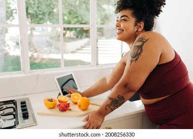 Happy Woman Standing With Fruits And Tablet Pc At Kitchen. Plus Size Female In Fitness Wear Making Healthy Food In Kitchen.