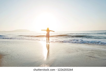 Happy woman standing on the beach with arms outstretched. - Shutterstock ID 1226203264
