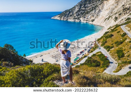 Happy woman standing on top of a rock with hat enjoying Myrtos Beach. Cephalonia island, Greece