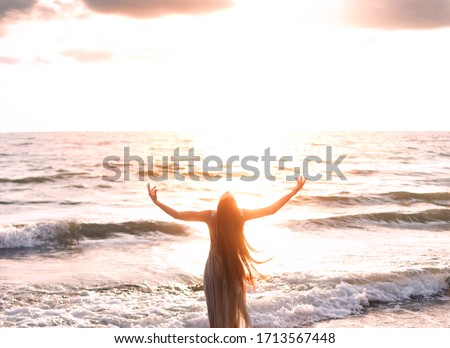 happy woman stands seashore turned away hand raised to heaven sky sun light. Lady girl enjoy sunny sunset sea waves. Concept hope divine pray freedom. Brunette long hair fluttering fly wind. Georgia