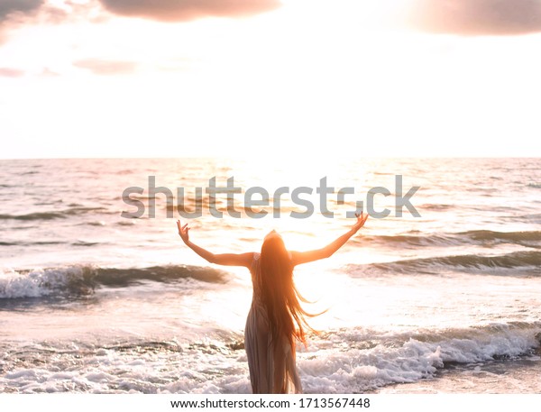 happy woman stands seashore turned away hand\
raised to heaven sky sun light. Lady girl enjoy sunny sunset sea\
waves. Concept hope divine pray freedom. Brunette long hair\
fluttering fly wind.\
Georgia