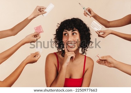 Happy woman in studio with hands offering birth control options. Woman smiles as she thinks about what choice to make for her body, she is deciding between hormonal and non-hormonal contraception.