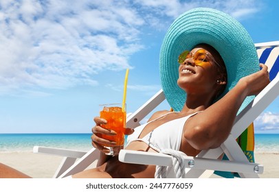 Happy woman is sunbathing on a beach deck chair, wearing sun hat and sunglasses, drinking a orange juice on a sunny day by the seaside, concept of a summer beach holiday, booking travel and resort  - Powered by Shutterstock