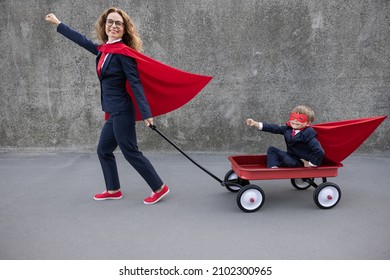 Happy Woman Superhero Going To Work. Funny Super Hero Kid Riding Retro Wagon. Happy Family Outdoor. Back To School And Business Concept