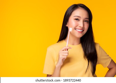 Happy woman take care tooth and holding toothbrush Young lady brushing her teeth Beautiful asian girl has beautiful tooth, white teeth   nice tooth alignment Yellow background, copy space Dental care
