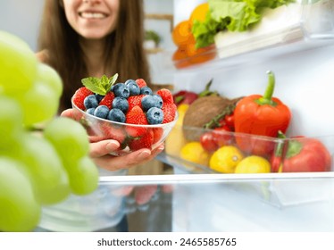 happy woman taking out a plate of berries from the refrigerator - Powered by Shutterstock