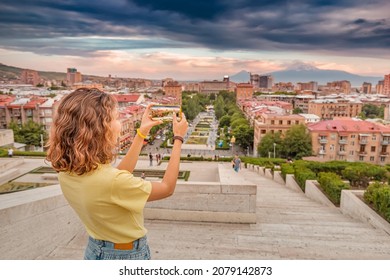 Happy woman taking pictures of a scenic urban landscape in Yerevan city with a distant view of famous Mount Ararat and Cascade complex