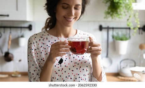 Happy woman taking tea break, holding glass mug, standing in kitchen, smelling and drinking hot aromatic beverage, enjoying morning and breakfast at home. Teatime, hygge, healthy lifestyle concept - Shutterstock ID 2062592330