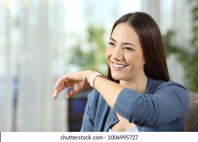 Happy woman talking to a smartwatch sitting on a couch in the living room at home - Powered by Shutterstock