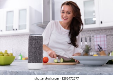 Happy Woman Talking To Voice Assistant While Slicing Cucumber With Kitchen Knife