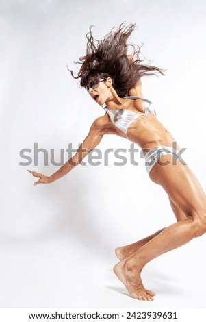 Happy woman with tanned skin and impressive muscular body is shaking arms and hair while posing with sunglasses on a white background in bikini. Fitness, bodybuilding, aerobics. Copy space, vertical.